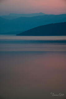 A minimalist fine art photograph of blue mountain silhouettes reflecting in pink twilight water.