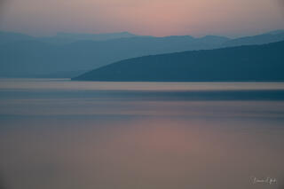 A minimalistic photograph y print of a French lake and it's surrounding mountains bathed in the pink and blue hues of sunrise.