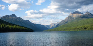 Panoramic view down Bowman Lake toward the Livingston Range, Glacier National Park, Montana, with forested shorelines and dramatic clouds.