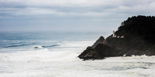 Heceta Head Lighthouse stands on a rocky headland above churning Pacific surf beneath an overcast sky, Oregon Coast fine art photography by Tamara Gooch.