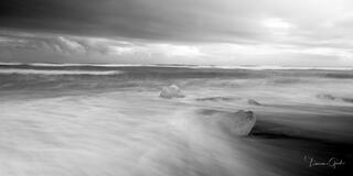Glacier ice chunks on Iceland's Diamond Beach, long exposure silky water swirling around ice, black & white fine art photography print by Tamara Gooch.