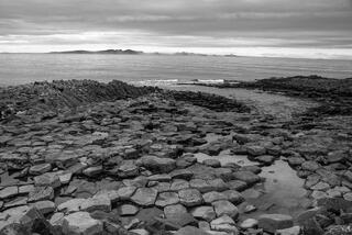 Black and white hexagonal basalt columns extending to dramatic overcast sea, south coast Iceland.