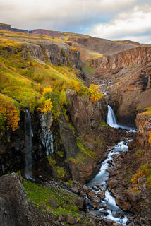 A vertical fine art photograph of Iceland in the fall with a beautiful waterfall cascading through a rocky canyon.