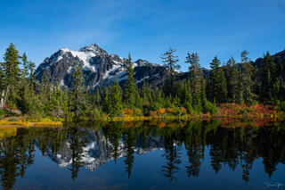 Mount Shuksan and autumn shoreline reflected in still waters of Picture Lake, North Cascades, Washington, under blue sky.
