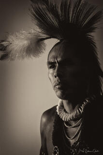 Native American man in porcupine roach headdress and bone breastplate, dramatic shadow, sepia fine art portrait by Tamara Gooch.