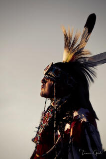 Native American man in feathered roach headdress and beaded regalia, profile view, golden backlight, fine art portrait photography by Tamara Gooch.