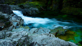 Long exposure fine art photograph of a turquoise waterfall rushing through mossy rocks in a Pacific Northwest forest.