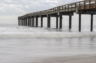 Florida pier extending diagonally across frame, long exposure silky surf around pilings, overcast sky, warm weathered wood, fine art photography by Tamara Gooch