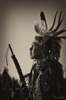 Native American elder in full war bonnet and ceremonial regalia, profile view, holding ceremonial staff, sepia-toned fine art portrait by Tamara Gooch.