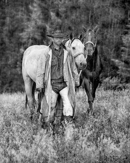 Black and white photograph of cowboy with two horses in falling rain Western lifestyle fine art photography