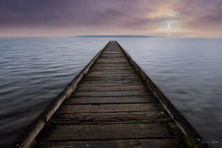 Weathered wooden dock extending to vanishing point over glassy water, soft purple and rose sunset sky, Pacific Northwest fine art print by Tamara Gooch.