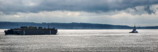 Cargo ship and tugboat on silver Puget Sound under dramatic storm clouds, Seattle, Washington.
