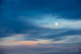 The full moon rising between the sunset colored clouds.