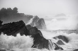 Storm waves washing over Shore Acres basalt rocks in black and white, sea mist filling air, evergreen trees barely visible, Oregon coast fine art photography.