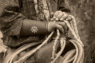 Close-up of cowboy hands holding rope with tooled leather cuff and silver concho, sepia-toned western fine art photography by Tamara Gooch.