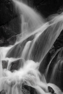 Black & white long exposure photograph of Yosemite waterfall cascading over dark rocks with silky smooth water motion, fine art nature photography print.