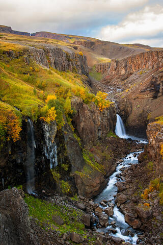 A vertical fine art photograph of Iceland in the fall with a beautiful waterfall cascading through a rocky canyon.