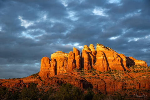 Color fine art photo of Cathedral Rock glowing deep amber in sunset light beneath a dramatic stormy blue sky, Sedona, Arizona.