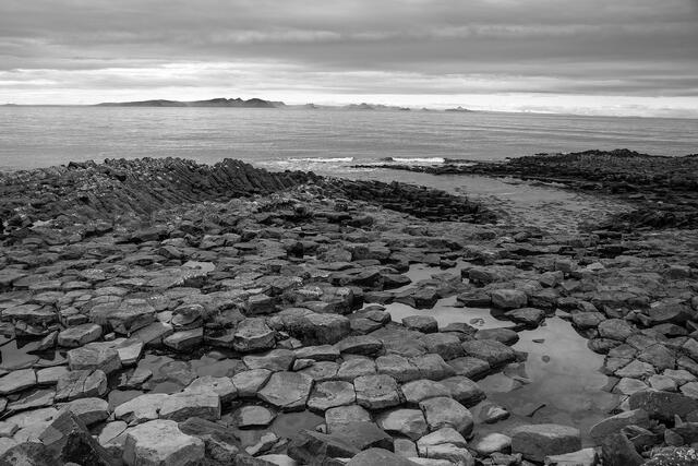 Black and white hexagonal basalt columns extending to dramatic overcast sea, south coast Iceland.