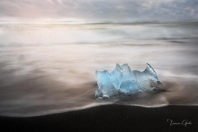 Single luminous blue glacier ice chunk on Iceland's Diamond Beach black sand, long exposure silky tide, soft warm sky, fine art photography by Tamara Gooch.
