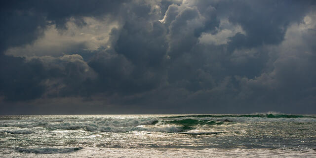 Dark towering storm clouds over Florida coast, shaft of light illuminating turquoise-green waves below, dramatic panoramic fine art photography by Tamara Gooch.